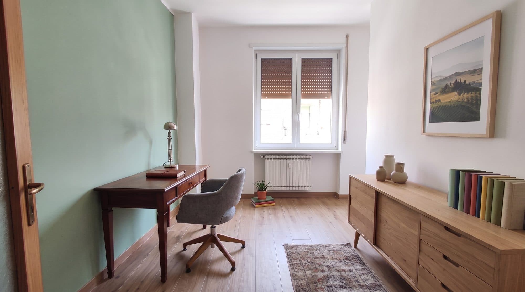 Studio ricavato in camera dopo la ristrutturazione: parete verde salvia, parquet chiaro e credenza in legno