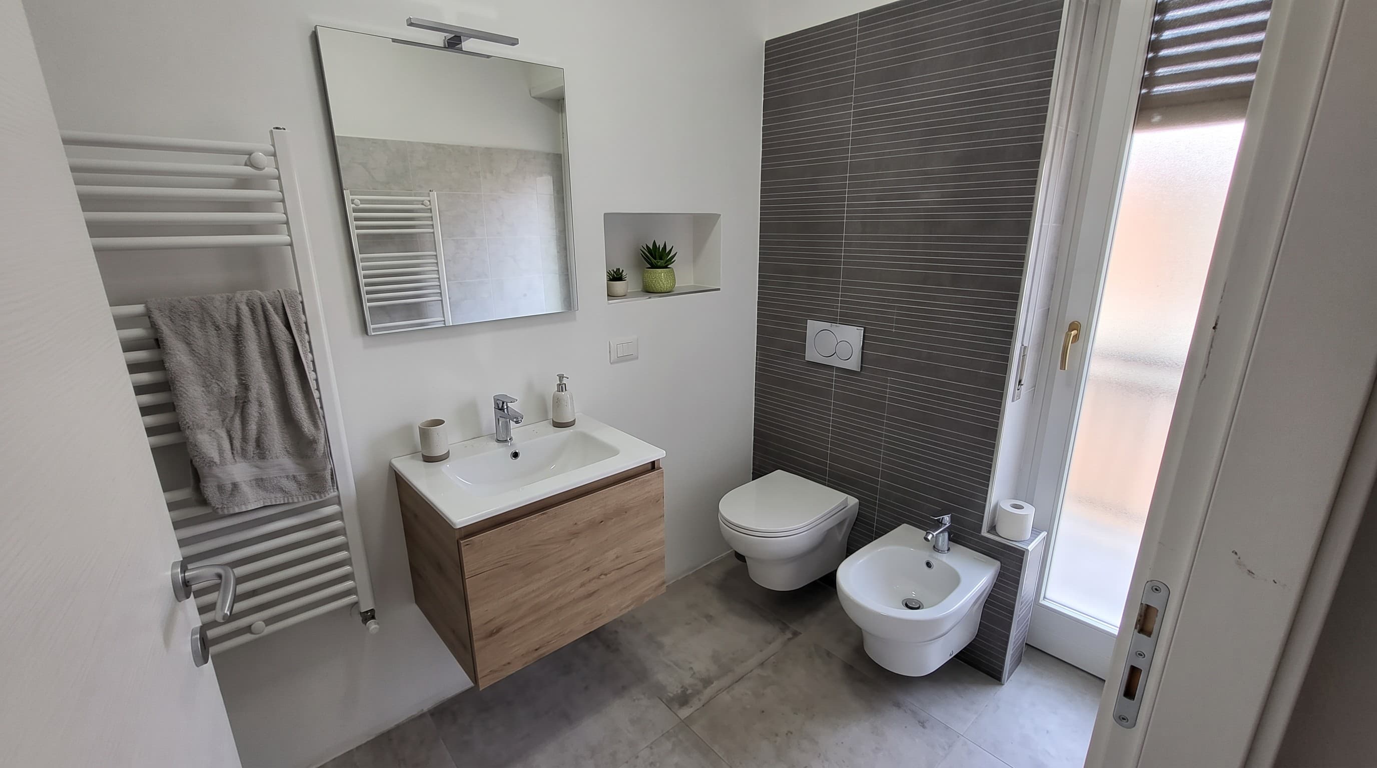 Bagno finito con mobile lavabo sospeso, specchio retroilluminato e parete a listelli scuri