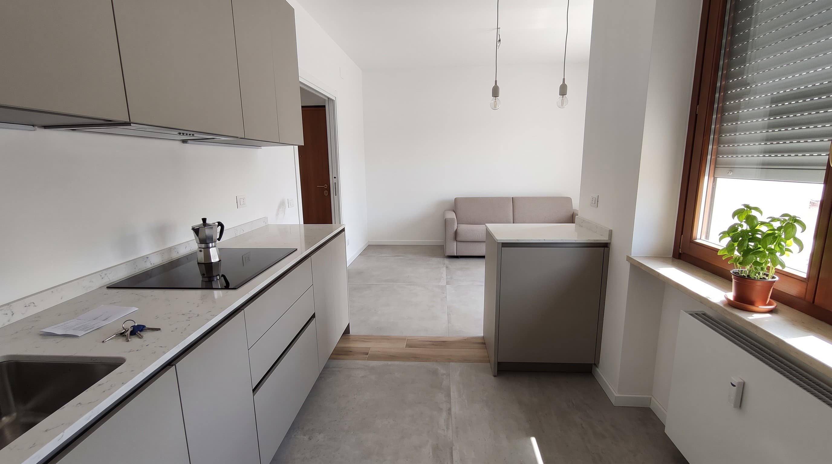 Cucina lineare bianca con piano scuro, aperta sul soggiorno, dopo il rifacimento