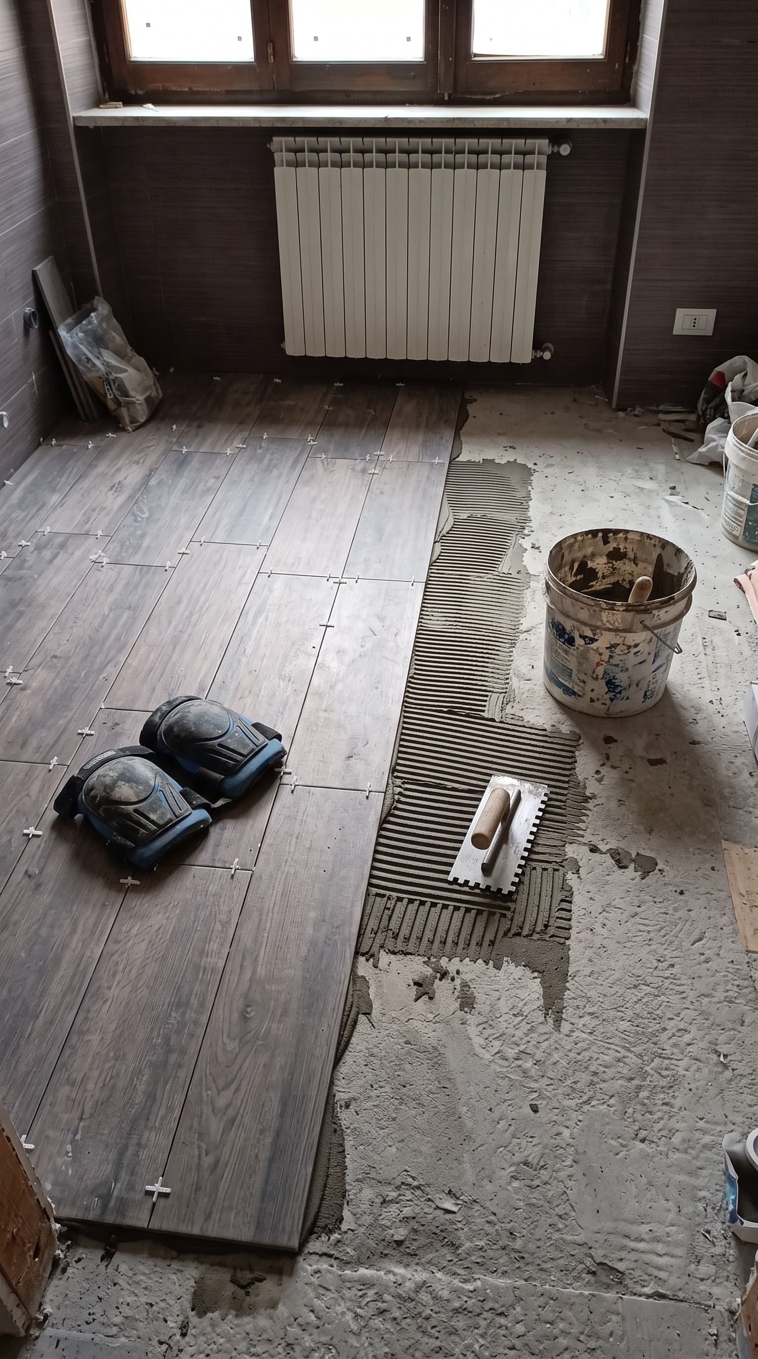 Posa del gres effetto legno: colla stesa a pettine, spatola e ginocchiere in cantiere
