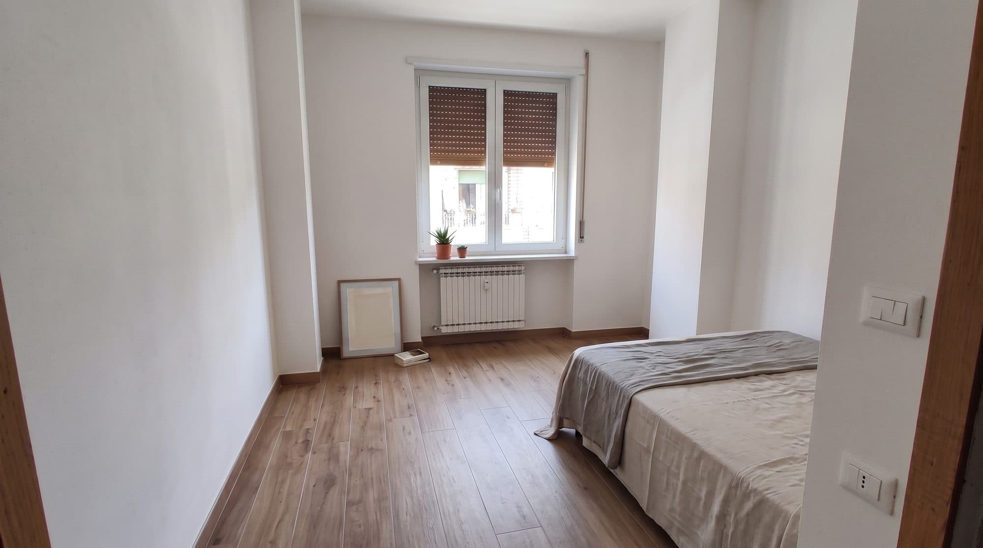 Camera da letto finita con parquet chiaro e termosifone nuovo sotto la finestra