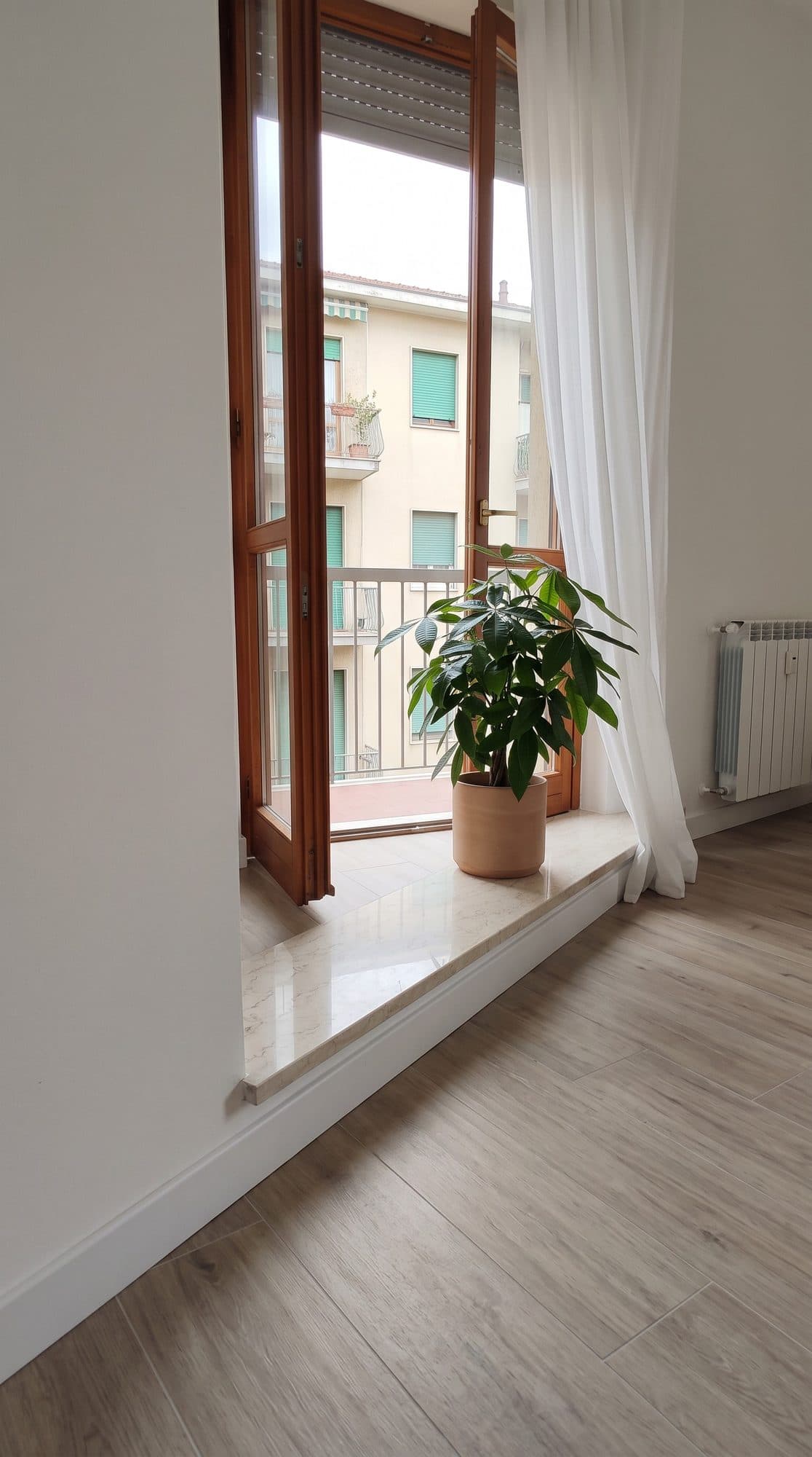 Portafinestra su balcone dopo i lavori, con termosifone nuovo e pavimento chiaro