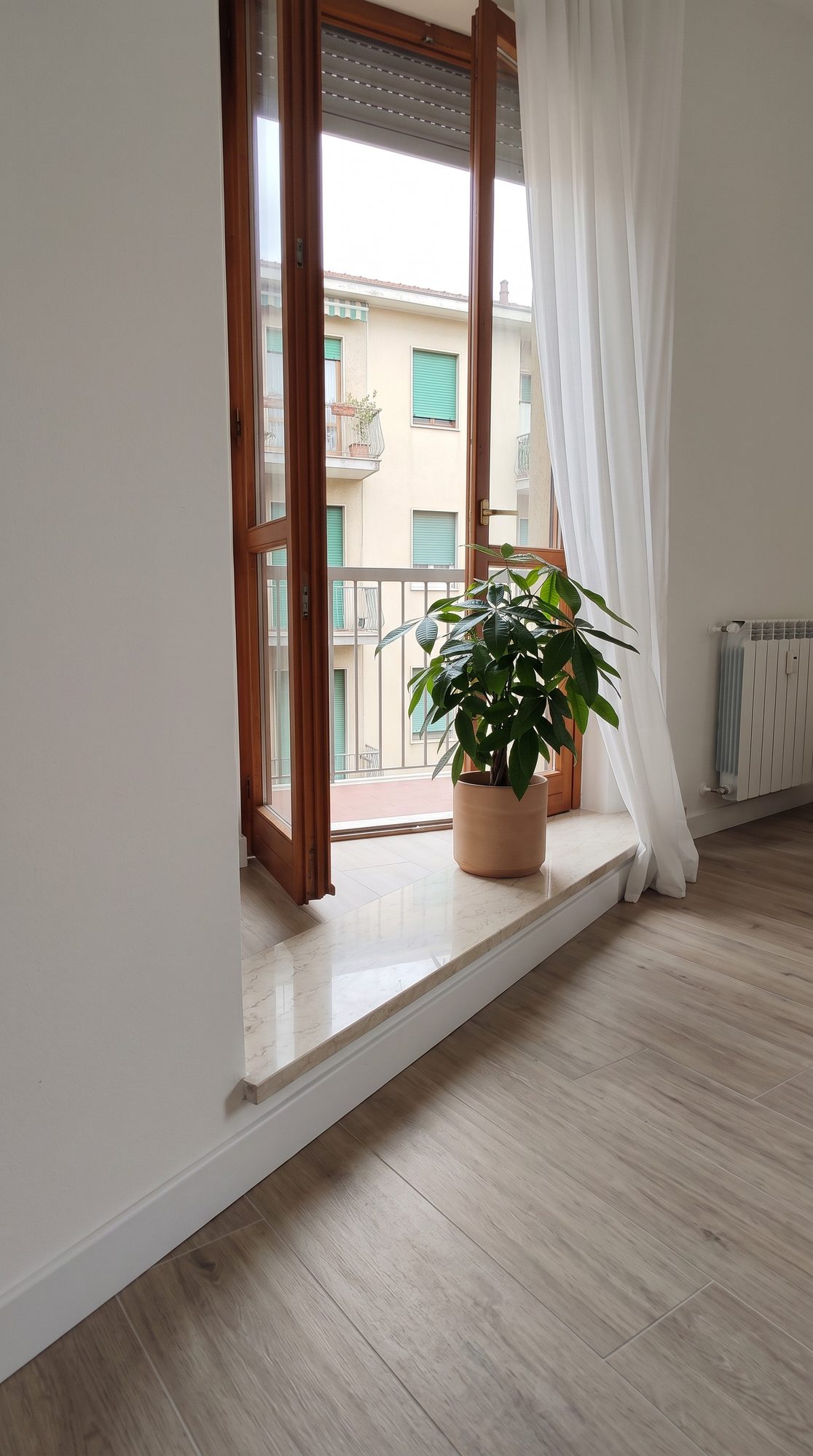 Portafinestra su balcone dopo i lavori, con termosifone nuovo e pavimento chiaro